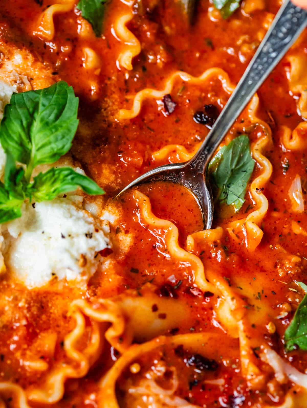 metal spoon dipping into lasagna soup filled with noodles and cheesy topping.
