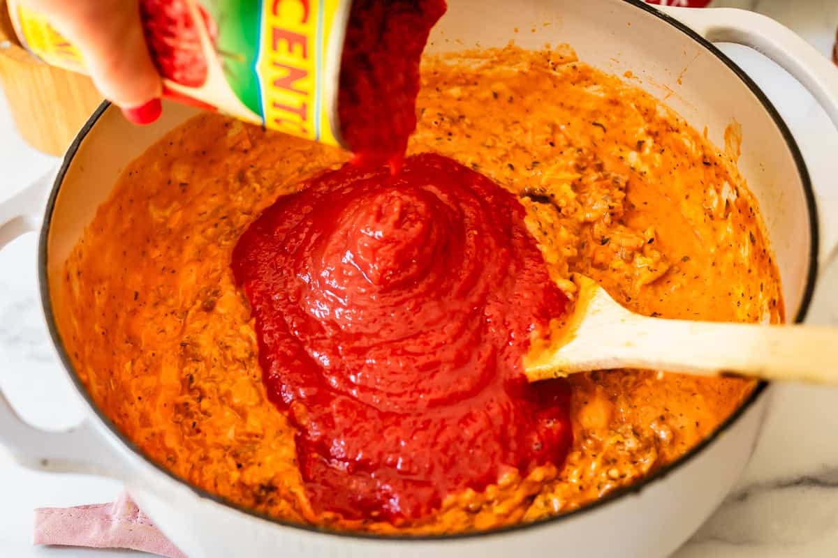 a hand pouring crushed tomatoes from a can into the soup pot.