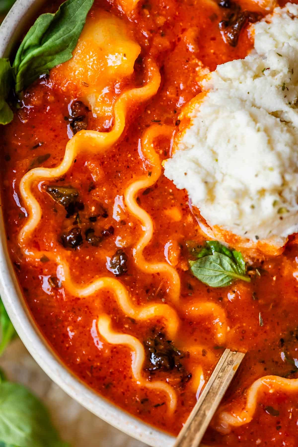 lasagna soup in a ceramic bowl with a soup spoon placed in it.