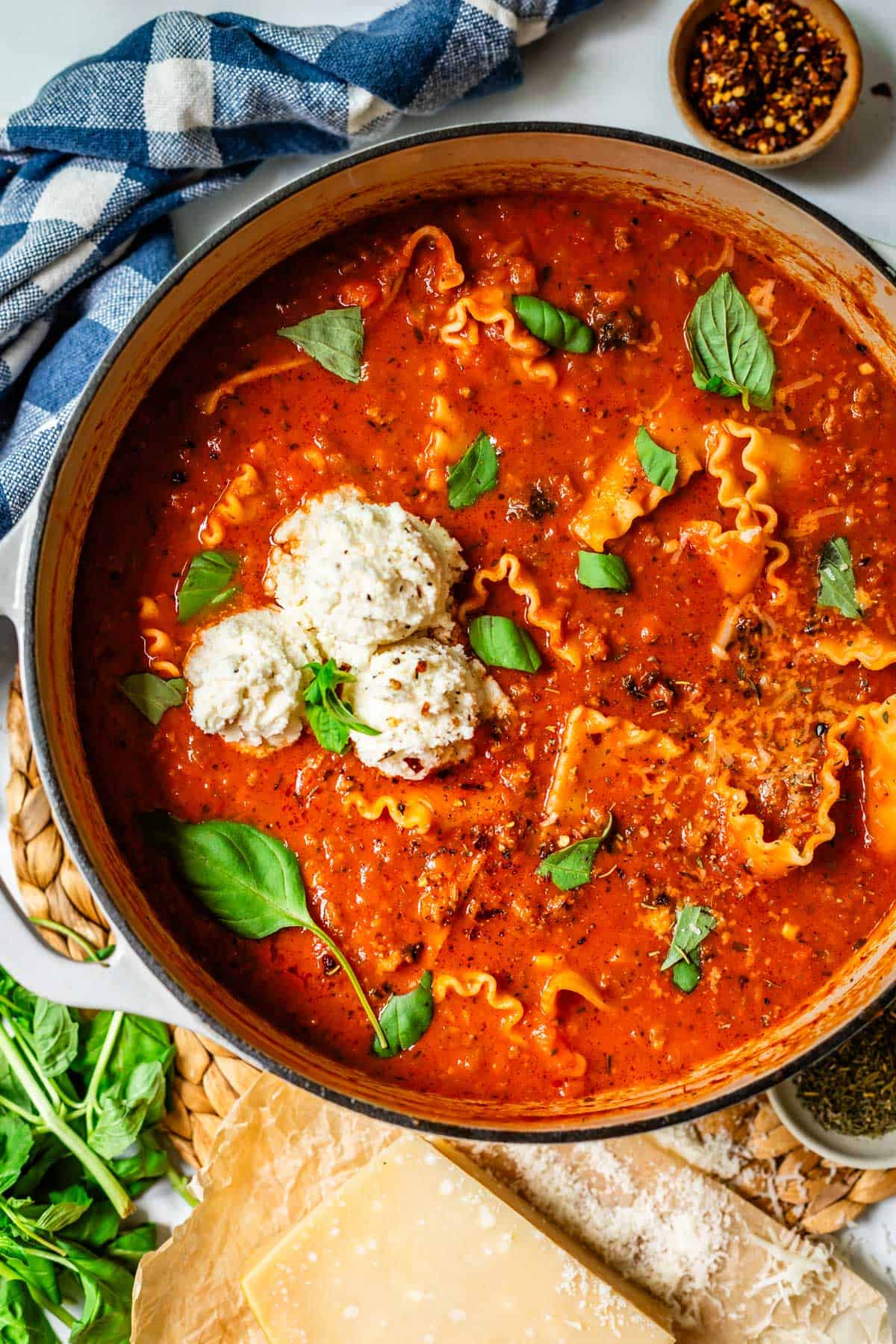 pot og lasagna soup sitting on a counter with extra basil and chili flakes next to it.