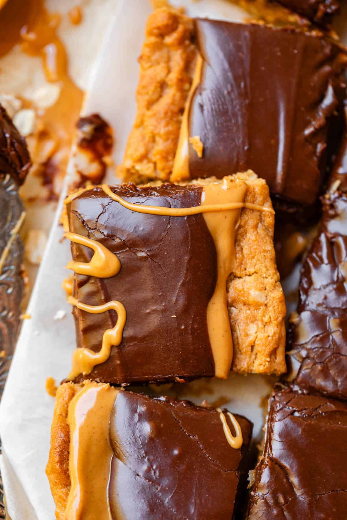 cut squares from peanut butter cookie bars on parchment paper with peanut butter drizzle.