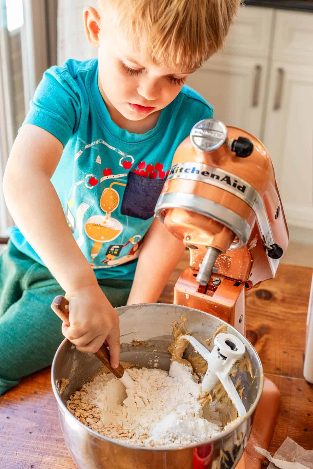 little boy using a spatula to mix flour into the oatmeal cookie dough.