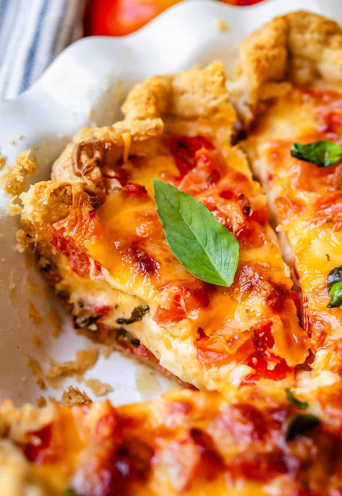 Close-up of slice of tomato pie with basil leaf in pie pan