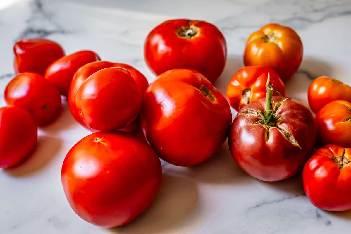 A bunch of tomatoe varieties including roma, heirloom, and vine laid out on marble.