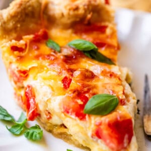 Slice of tomato pie on plate with basil.