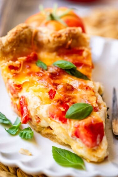 Slice of tomato pie on plate with basil.