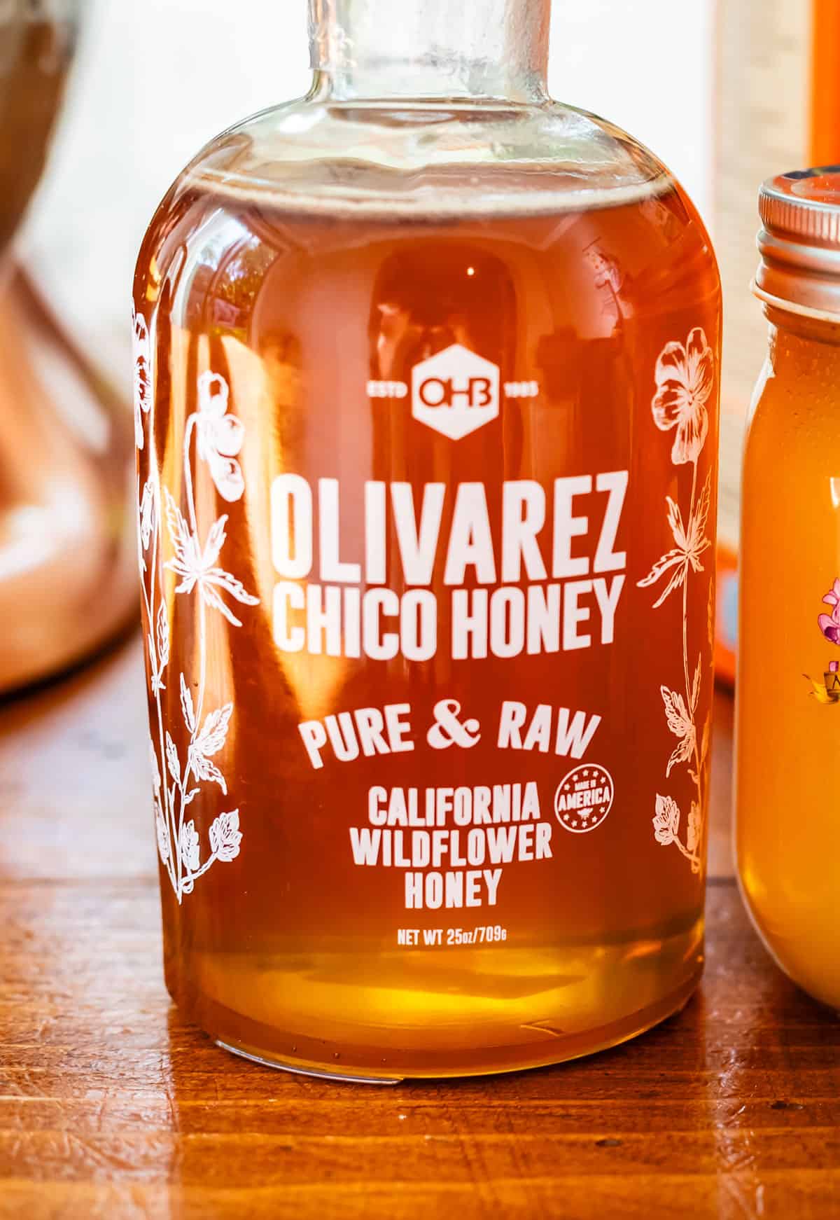 a glass bottle of Olivarez pure raw hpney on a wood table.