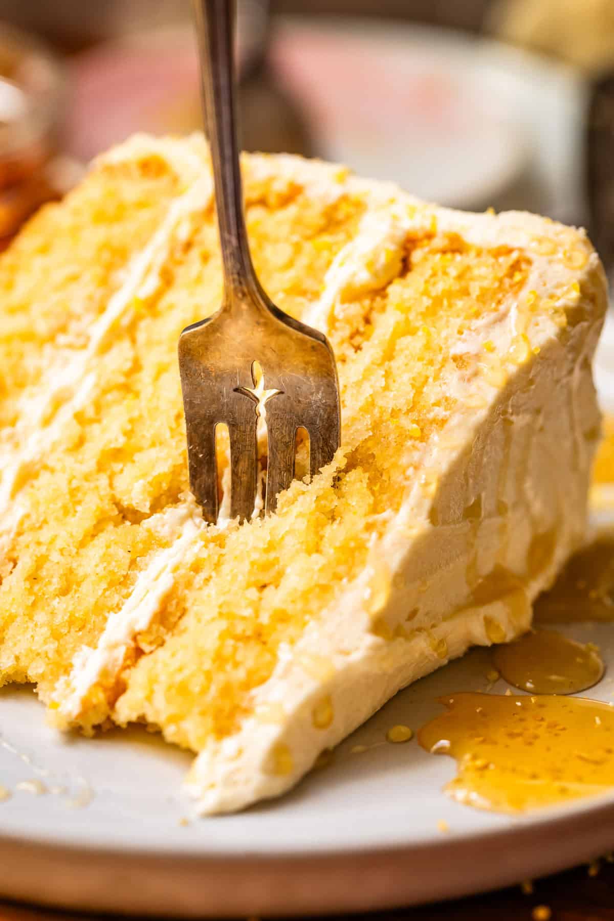 fork standing in the middle of a piece of cornbread cake with whipped frosting.