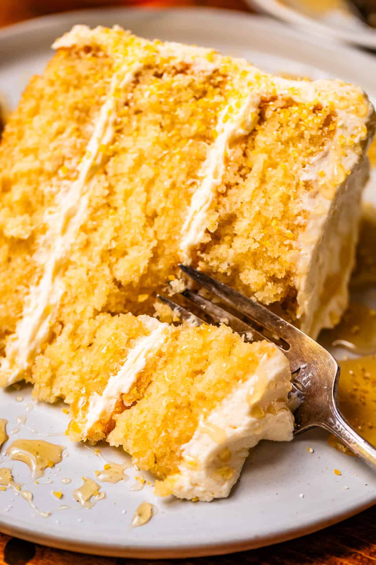 fork cutting into a pieve of cornbread cake with honey frosting.