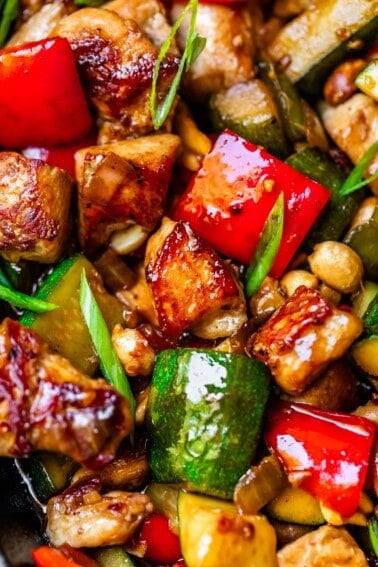 close up of seared chicken, red bell peppers, green onions, in a Kung Pao sauce.