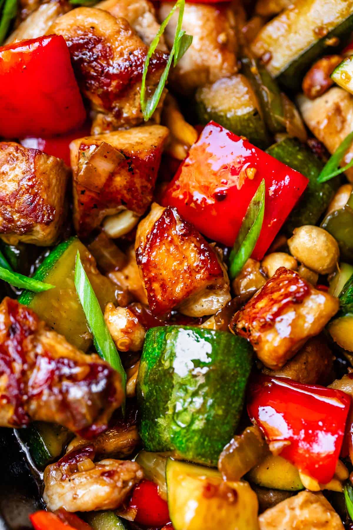 close up of seared chicken, red bell peppers, green onions, in a Kung Pao sauce.