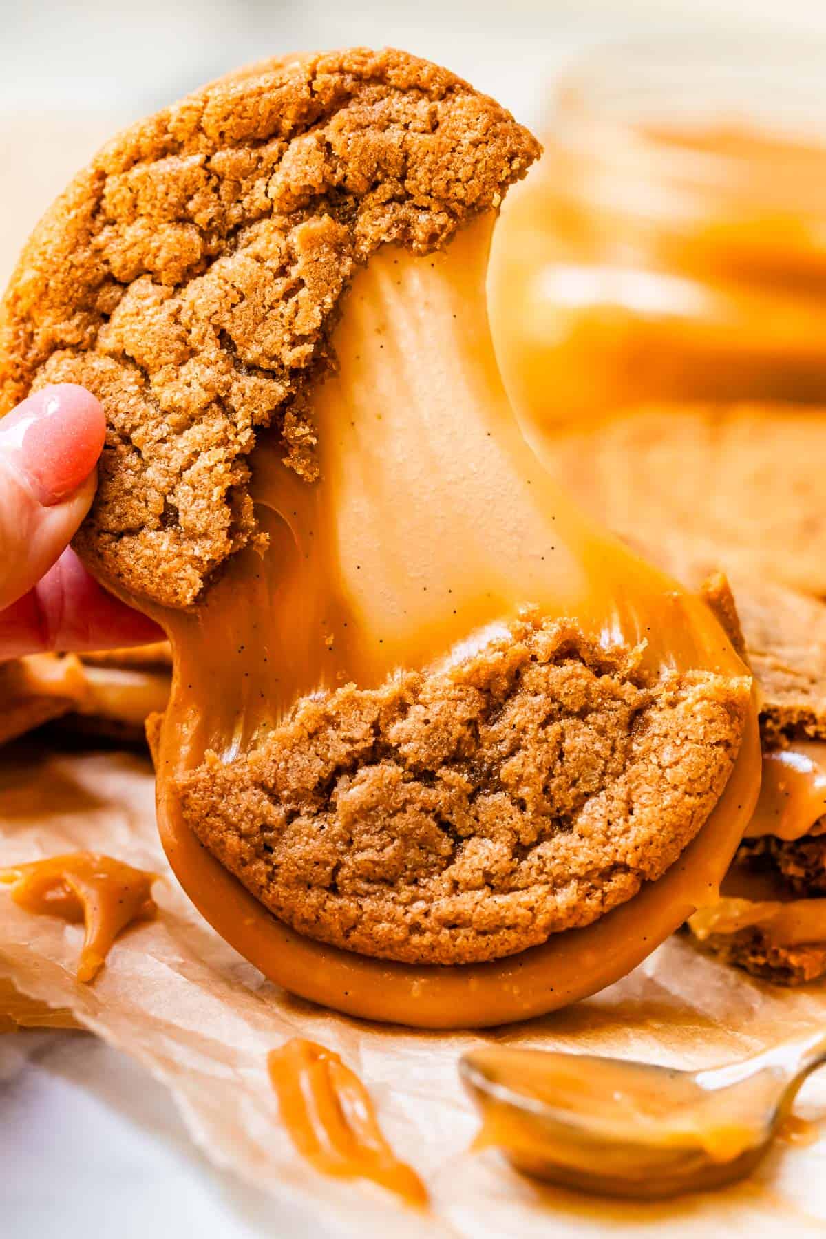 hand pulling the top half of a sandwich cookie away form the bottom showing a caramel stretch.