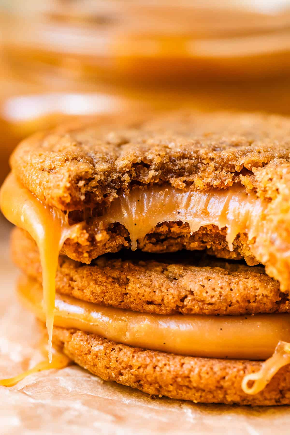 salted caramel cookie sandwich with a bite taken from it on top of another cookie sandwich.