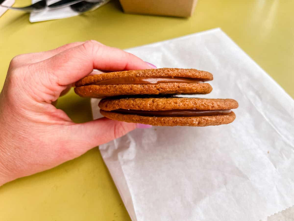 two salted caramel sandwich cookies held in a hand on a table.