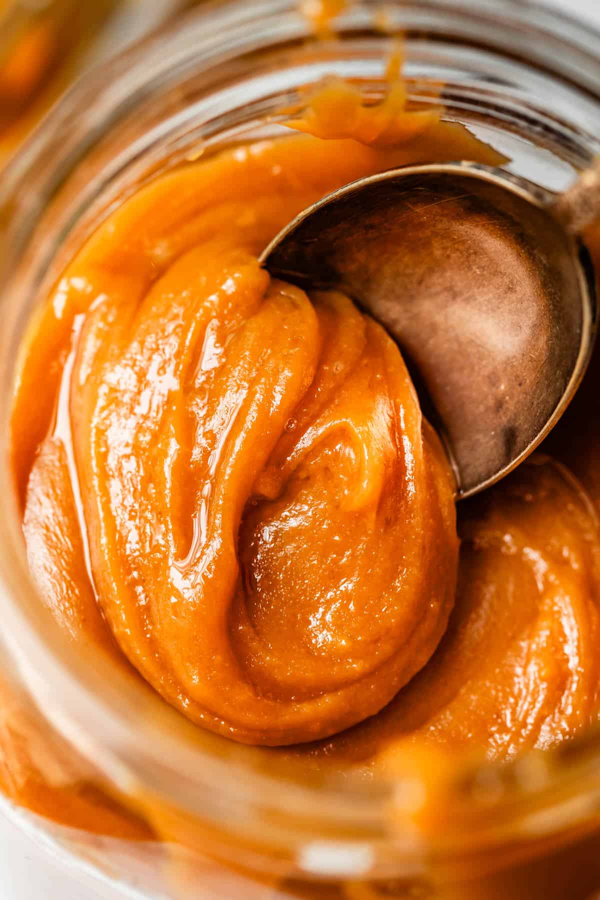 metal spoon dipping into a glass jar to get a scoop of caramel.