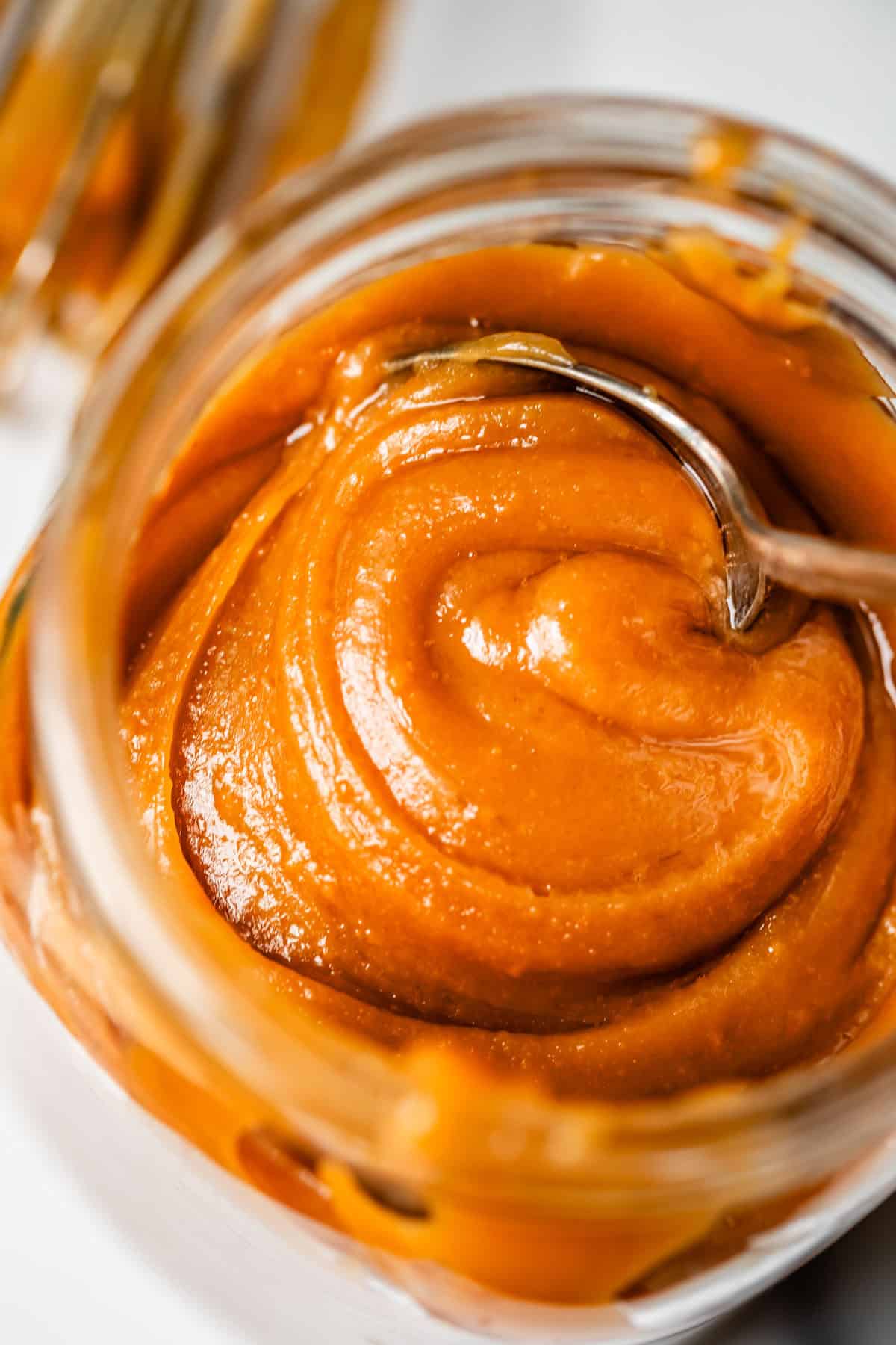 metal spoon digging into salted caramel from a glass mason jar.