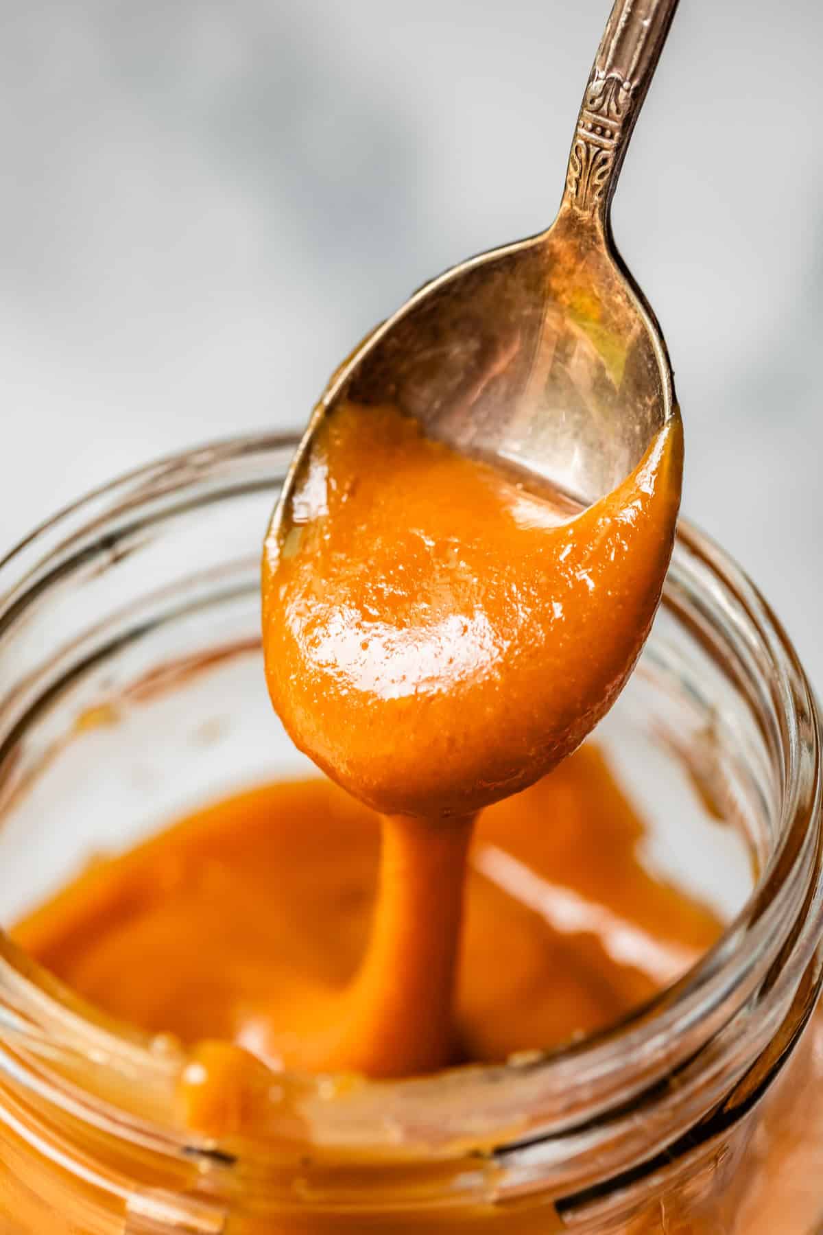 metal spoon dripping thick and creamy salted caramel from it into a jar.