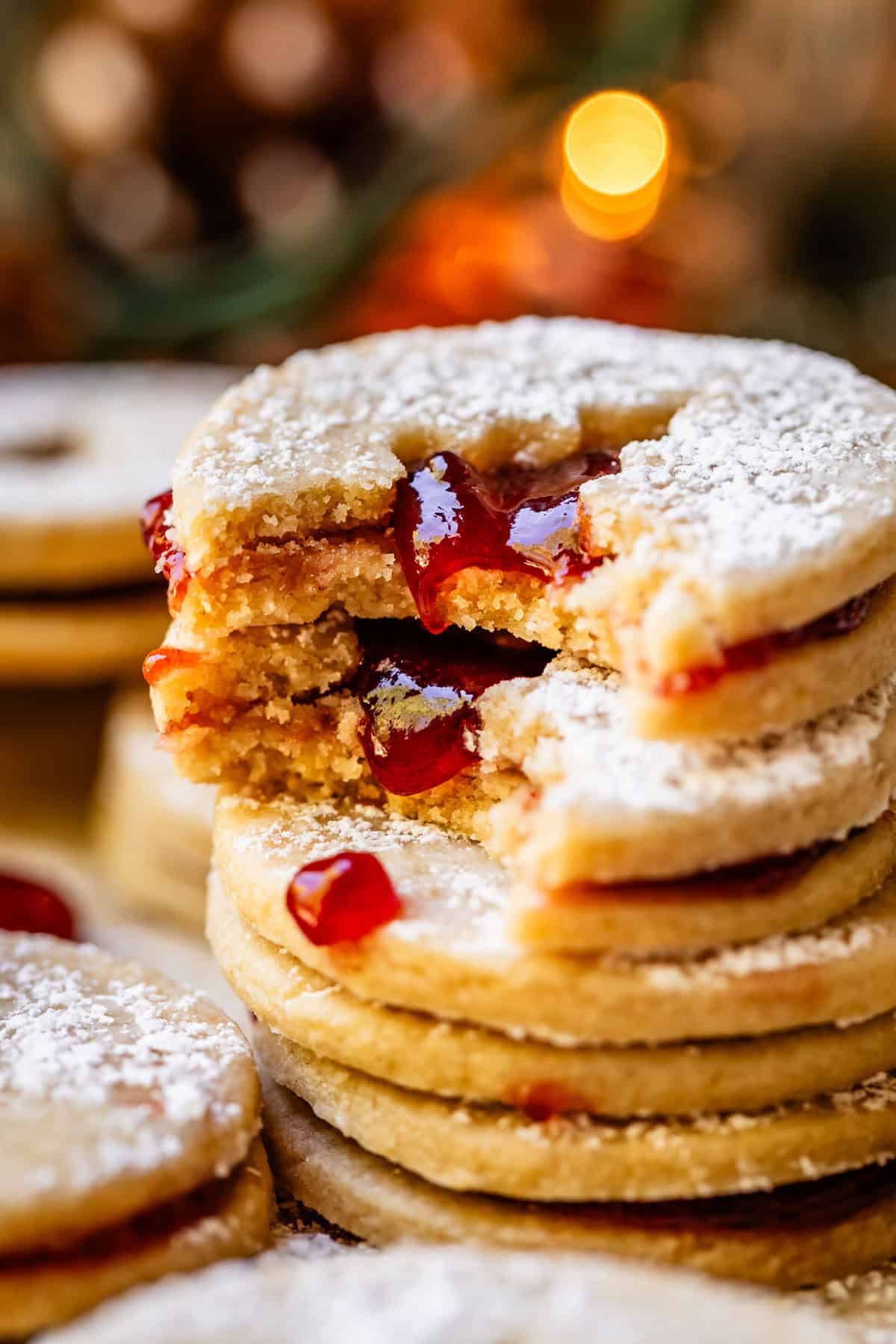 stack of jam cutout linzer cookies with christmas lights in the background.