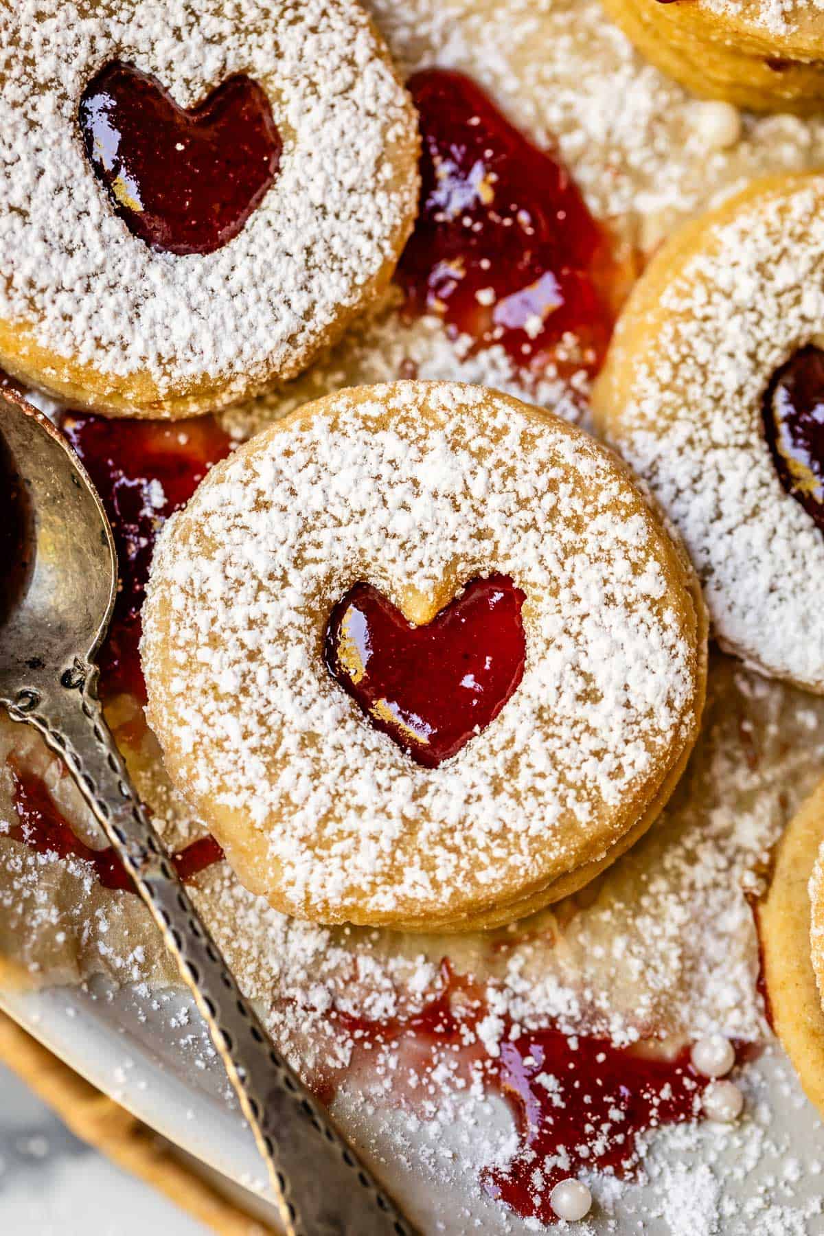 three linzer cookies with a cutout heart in the center, lightly dusted with powdered sugar.