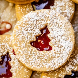 linzer cookie filled with raspberry jam peeking through a Christmas tree cutout.
