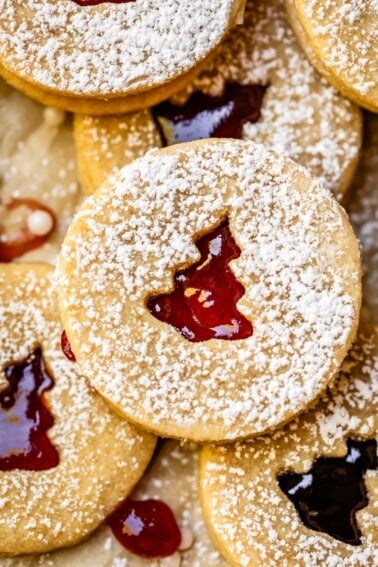 linzer cookie filled with raspberry jam peeking through a Christmas tree cutout.