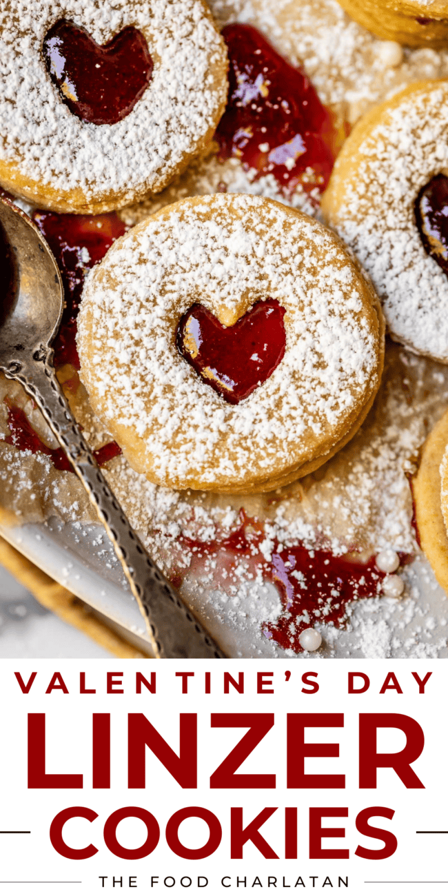 heart shaped linzer cookies with raspberry jam and metal spoon.