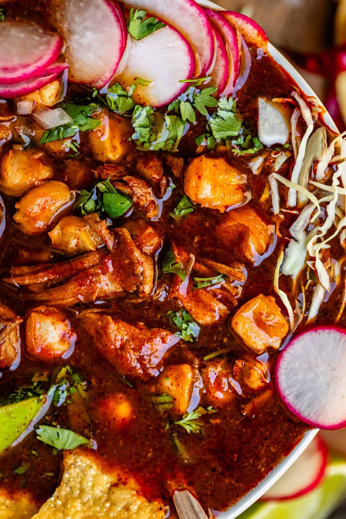 bowl of pozole with pork and hominy, and radish, cabbage, and cilantro topping.