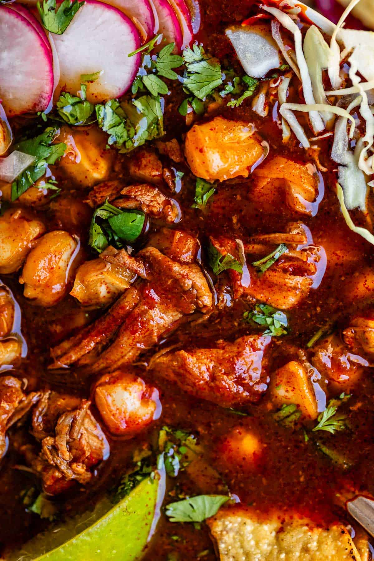 close up of pozole rojo showing the bits of tender pork, hominy, and toppings.