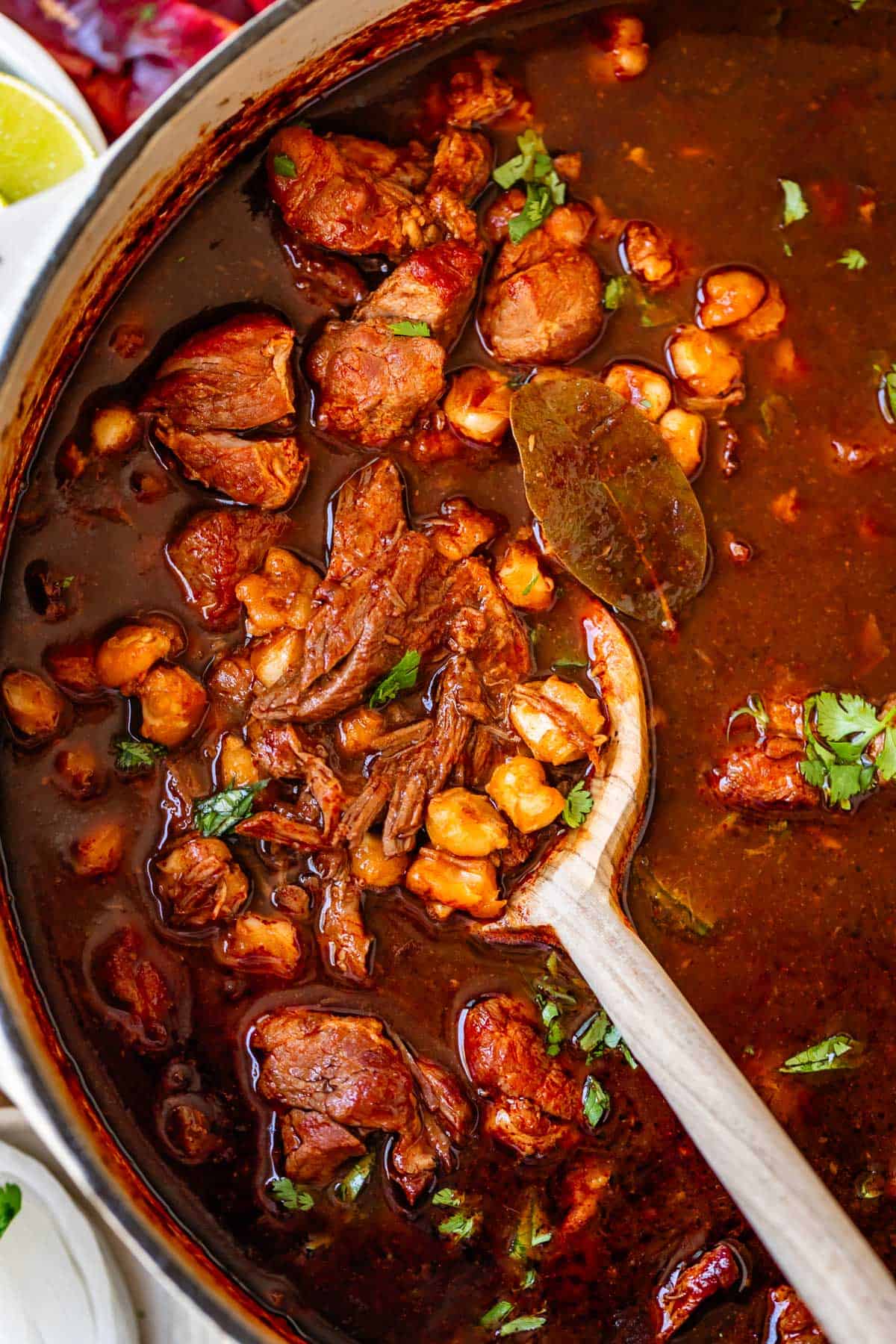 large dutch oven pot filled with pozole rojo soup with a large wooden spoon stirring.