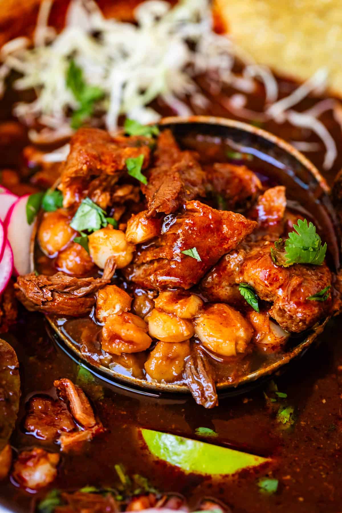 metal ladle lifting up pork and hominy red pozole with cilantro garnish from the pot.