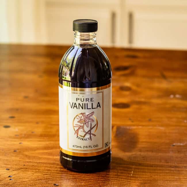 Container of pure vanilla extract on wooden table.
