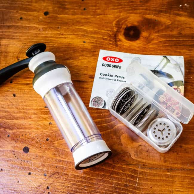 OXO cookie press and inserts with instructions on a wooden table.