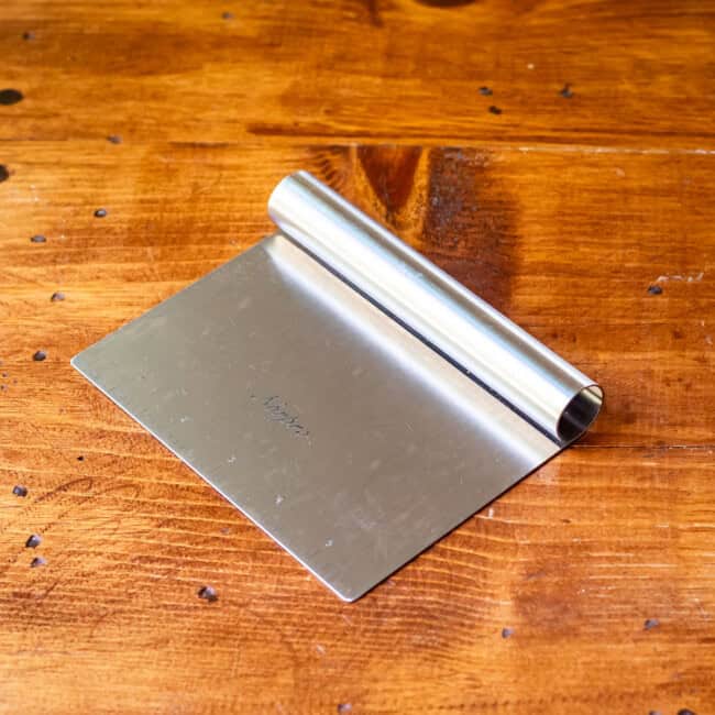 Norpro stainless steel kitchen scraper on wooden table.