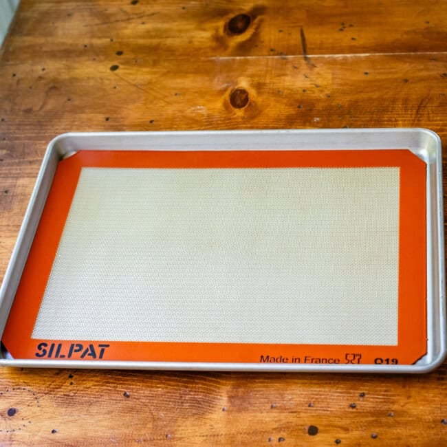 Silpat silicone baking mat on half sheet baking pan on wooden table.