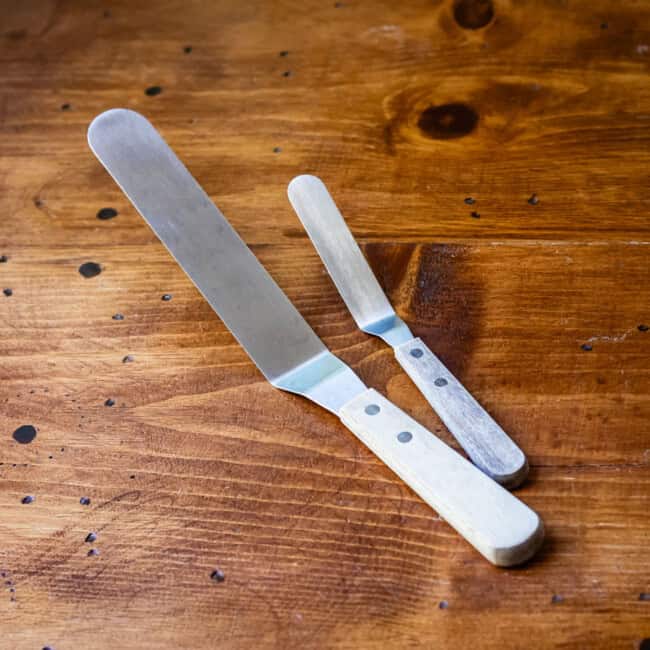 Large and small offset spatulas on wooden table.