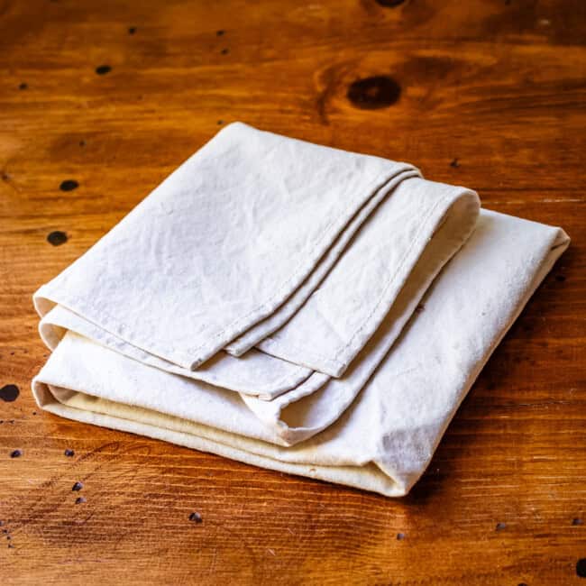 Large pastry cloth folded up on wooden table.