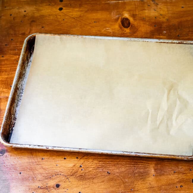Pre-cut parchment paper sized for a half-sheet pan on a half sheet baking pan on a wooden table.