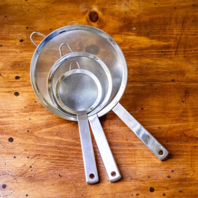 Three sizes of mesh strainers stacked on wooden table.