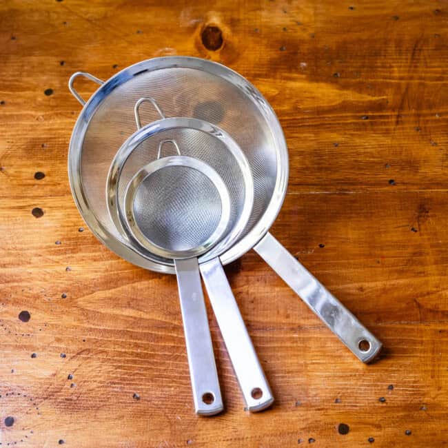 Three sizes of mesh strainers stacked on wooden table.