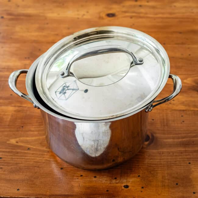 Large stainless steel stockpot with copper lining on wooden table.