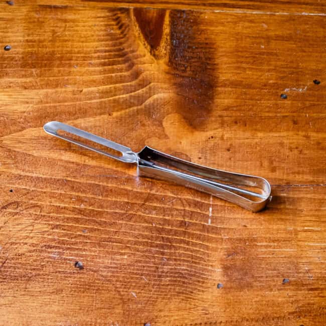Simple metal kitchen peeler on wooden table.