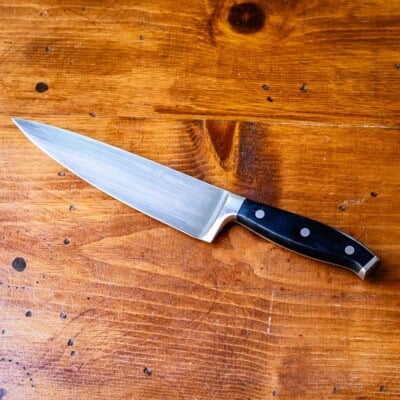 Chef's knife with riveted handle on wooden table.