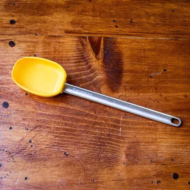 Scooping rubber spatula with metal handle on wooden table.