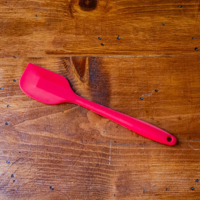 Hard rubber red spatula on wooden table.