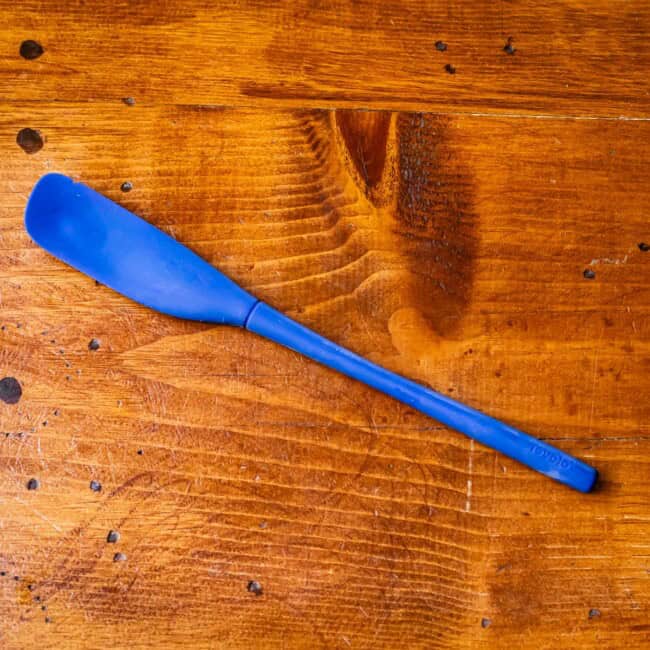 Long, thin blue rubber spatula on wooden table.