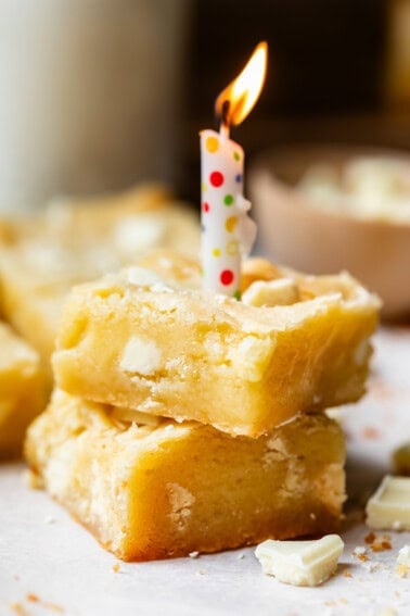 two white chocolate brownies stacked on each other, with a lit birthday candle in the top one.
