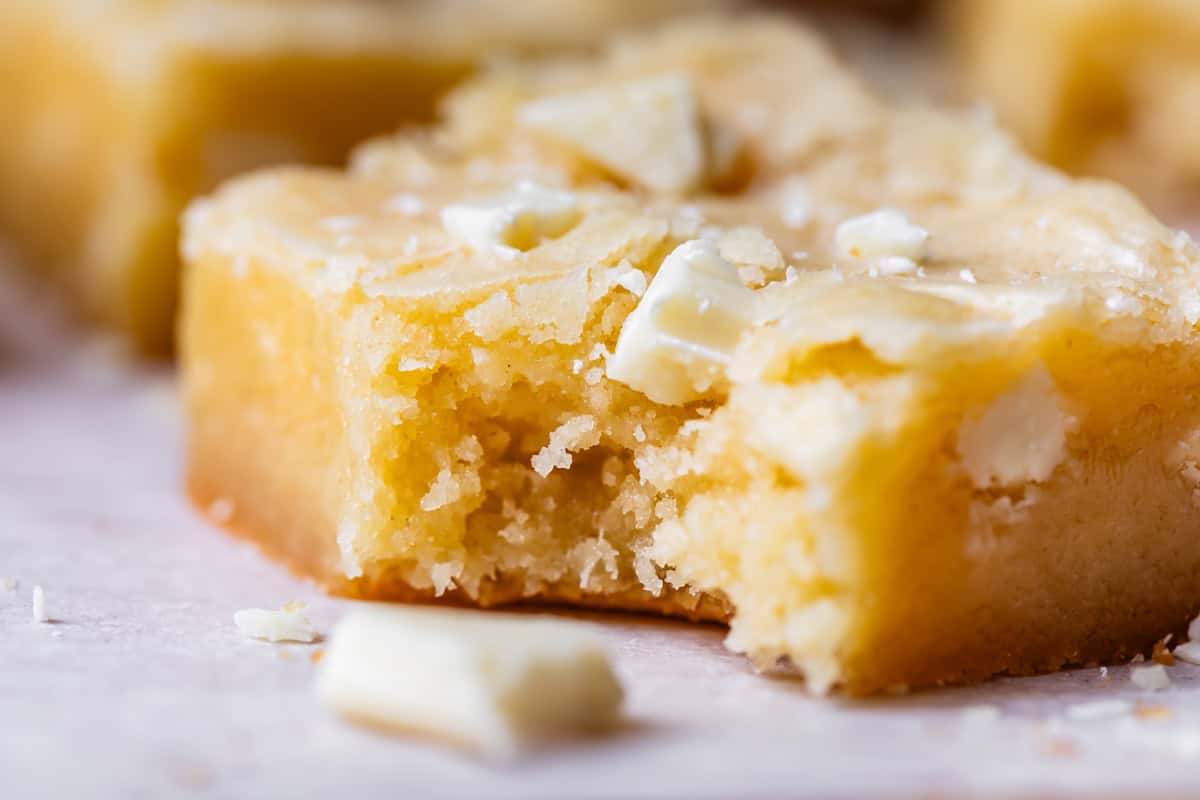 close up side view of white chocolate brownies with a bite missing and white chocolate on top.