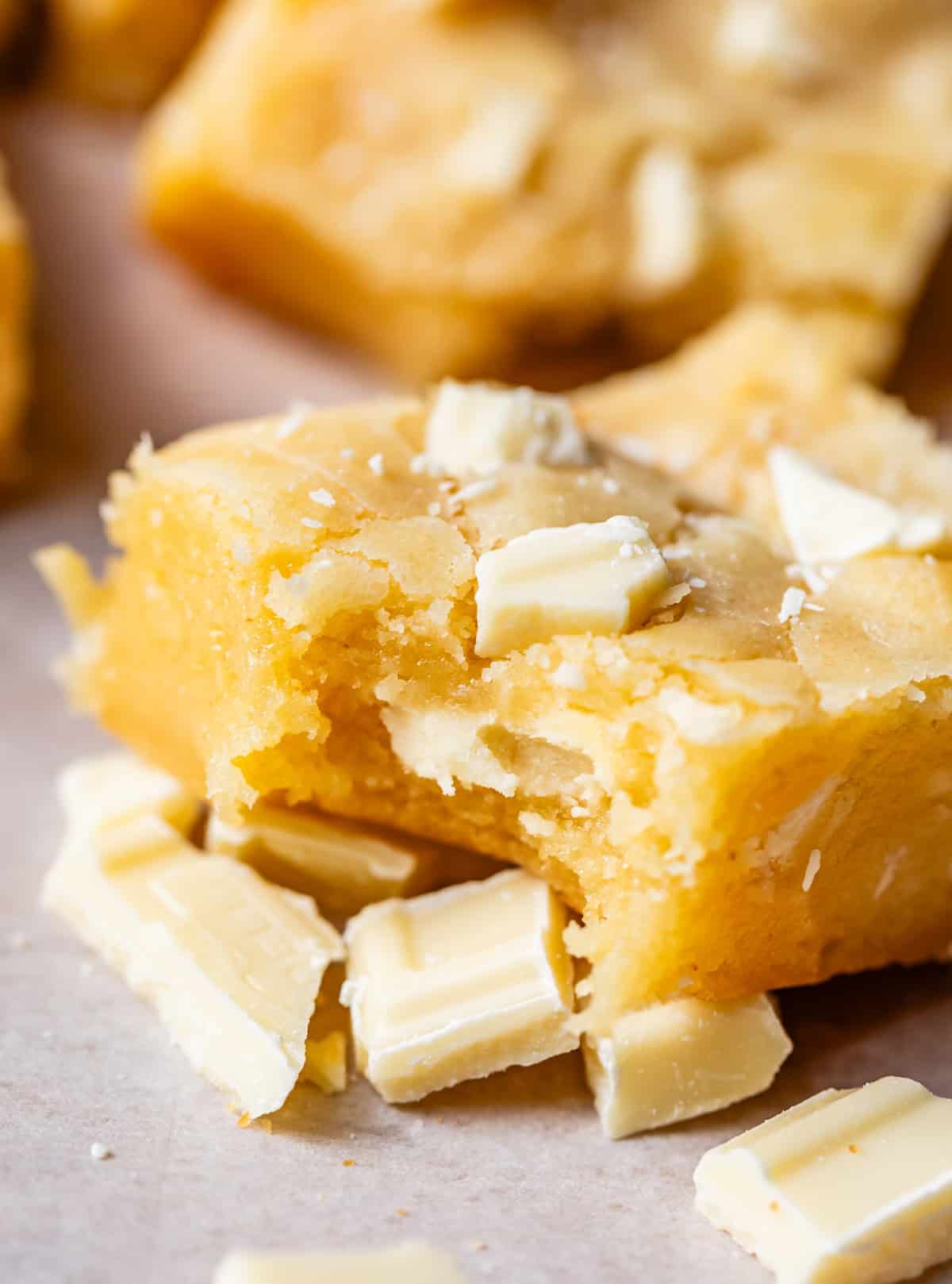 a piece of white chocolate brownies with a bite taken, sitting on chopped white chocolate.