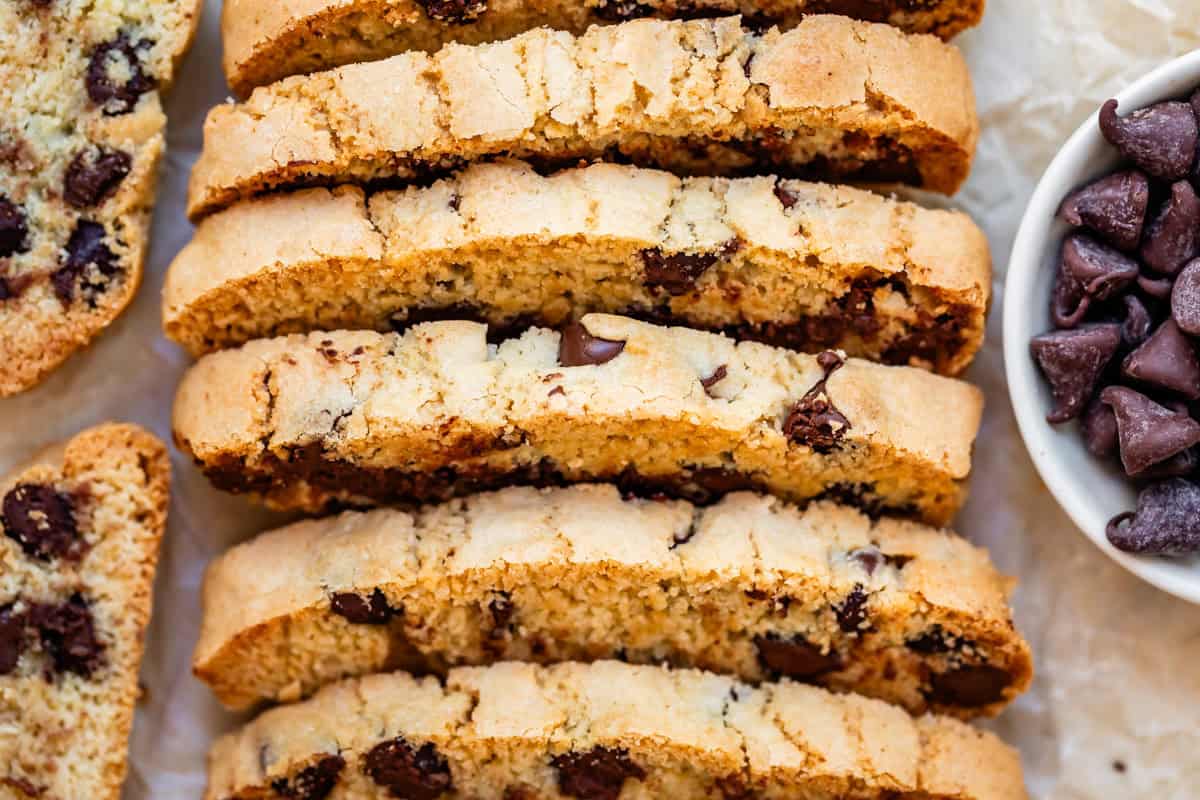 close up several stacked pieces of baked biscotti next to a bowl of chocolate chips.