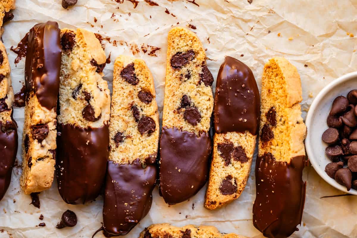 7 pieces of baked biscotti dipped in chocolate on one end sitting on parchment paper.